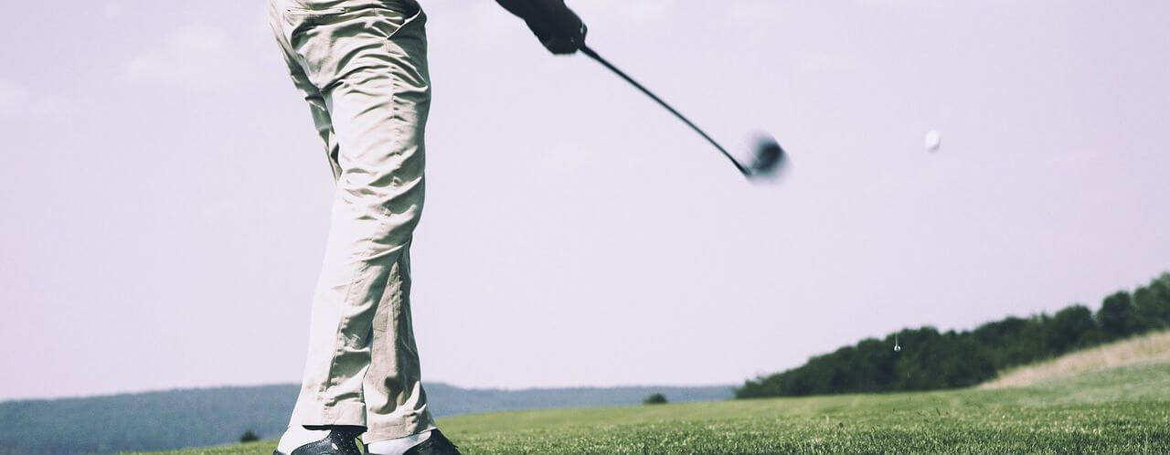 man swinging a gold club on a course
