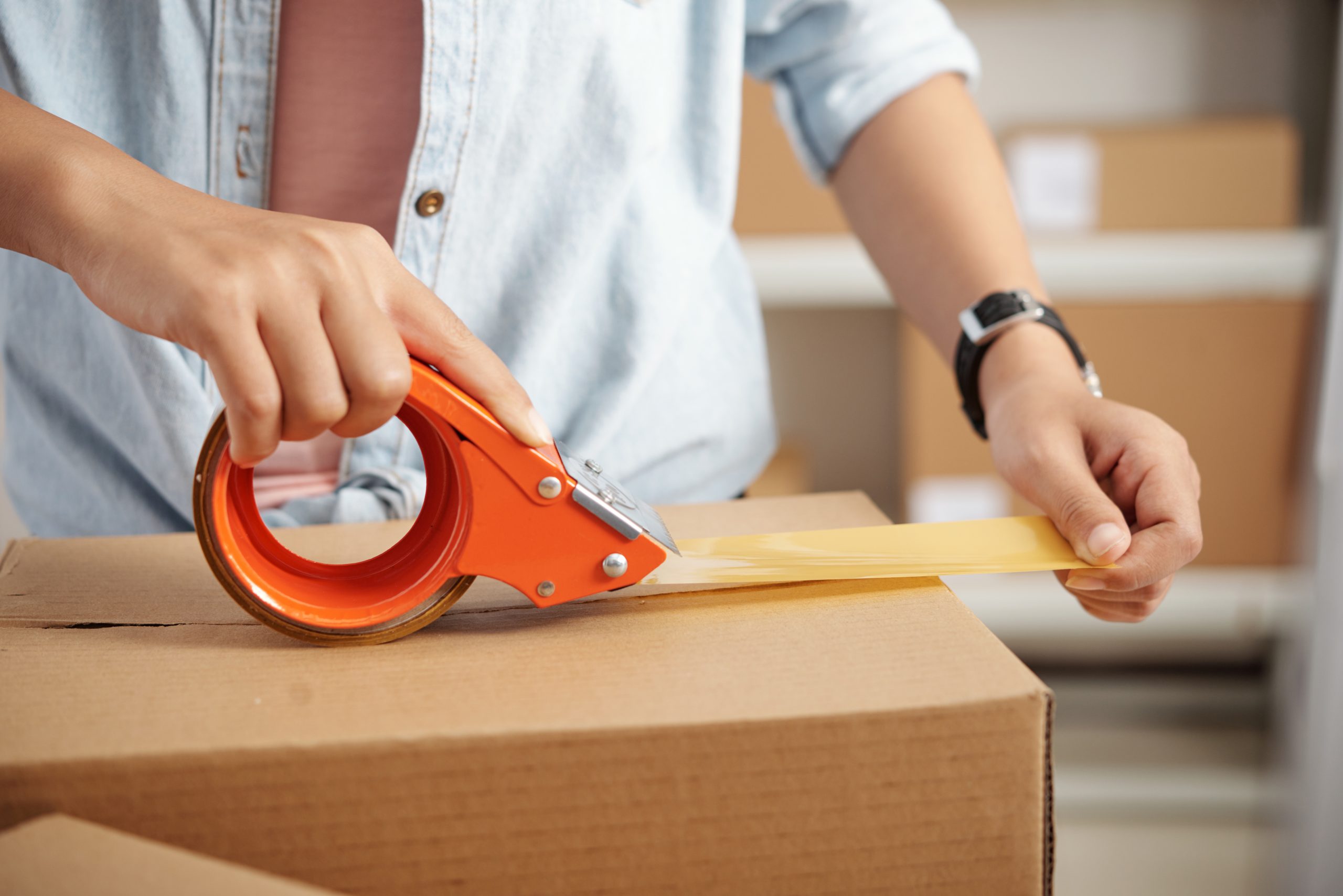 Close-up of female hands packing cardboard box with scotch
