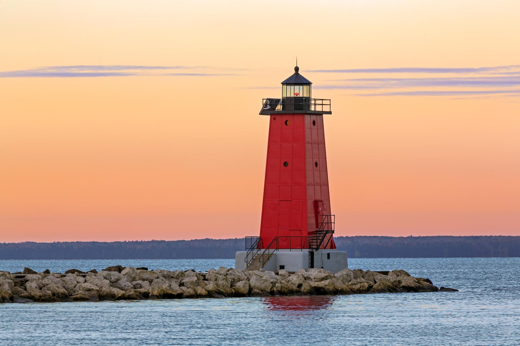 The sky glows with color as the sun rises on the red lighthouse at Manistique on the Lake Michigan Coast of Michigan's Upper Peninsula.